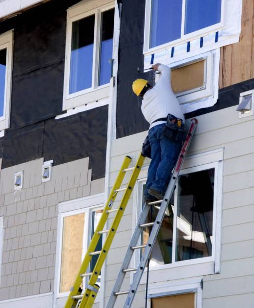 Consctruction worker hanging siding on new apartment building under consctruction.